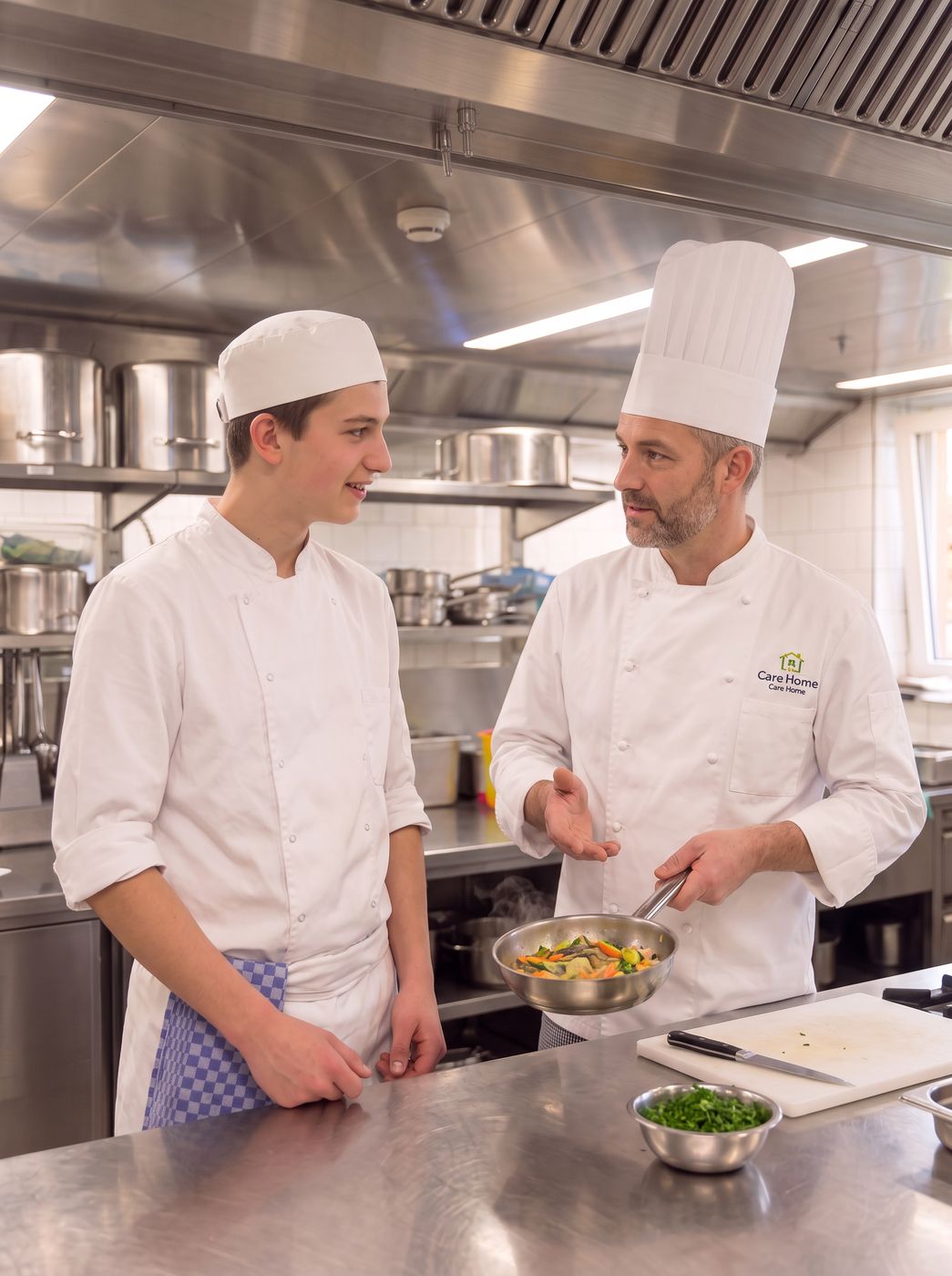 Küchenchef erklärt einem jungen Koch in der Küche ein Gericht