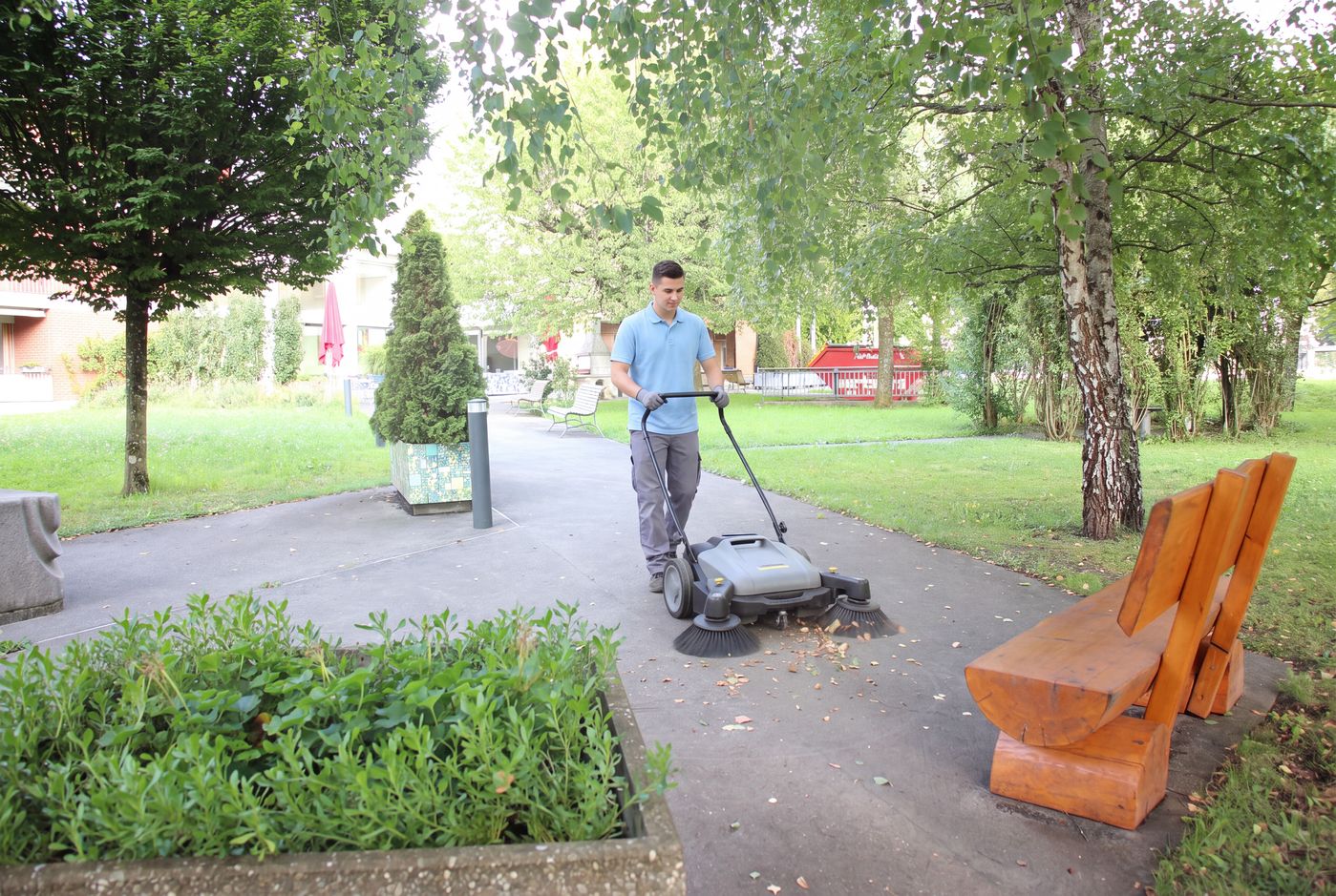 Junger Mann reinigt den Gartenweg mit einer Kehrmaschine